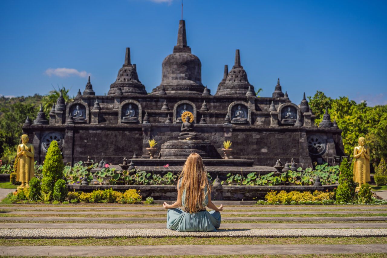 Vrouw zit voor een prachtige boeddhistische tempel in meditatiehouding
